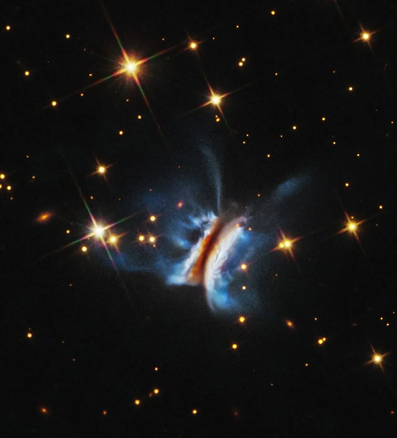 Hubble image of the edge-on protoplanetary disk IRAS 23077+6707, nicknamed Dracula's Chivito, showing a dark central dust lane between two glowing nebulae with wispy filaments.